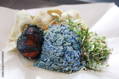 Photography A delicious serving of Malaysian Nasi Kerabu featuring blue pea flower rice served with grilled chicken, raw vegetable and herb salad (ulam), and fish crackers