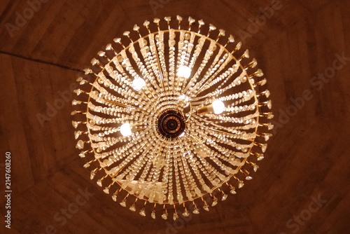 Bottom-up view of a large luxurious crystal chandelier with glowing warm lights.