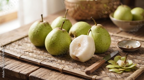 Fresh Pears on a Table: A collection of ripe, green pears, with one sliced in half to reveal its juicy white flesh, are artfully arranged on a woven mat on a rustic wooden table.