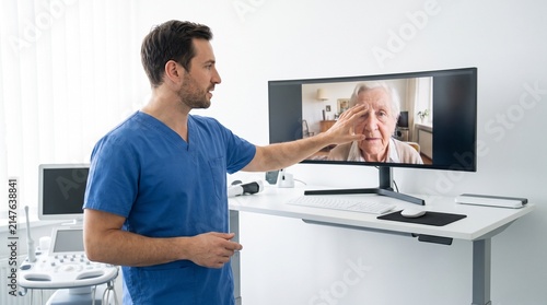 Doctor consulting with elderly patient via video call in modern clinic.