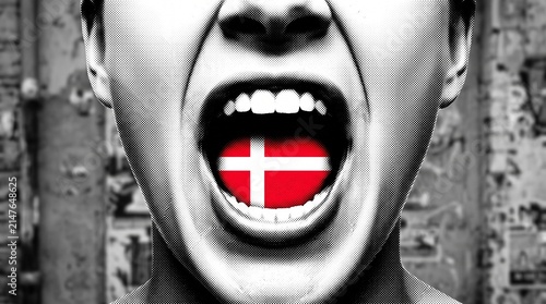 A black and white close-up of a person's face with their mouth wide open, revealing a vibrant Danish flag inside, against a textured background.
