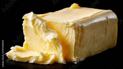 Close-up of fresh creamy yellow butter block with a slice cut out isolated on a black background