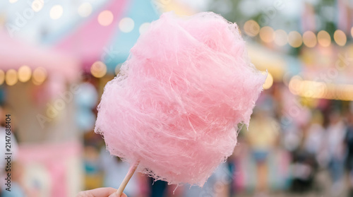 Close-up of a fluffy pink cotton candy being held on a stick at an outdoor festival.