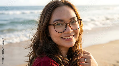Young woman with glasses smiling on a sunny beach with ocean in the background