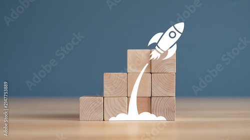 A white rocket icon launches from a stack of wooden blocks against a dark blue background.