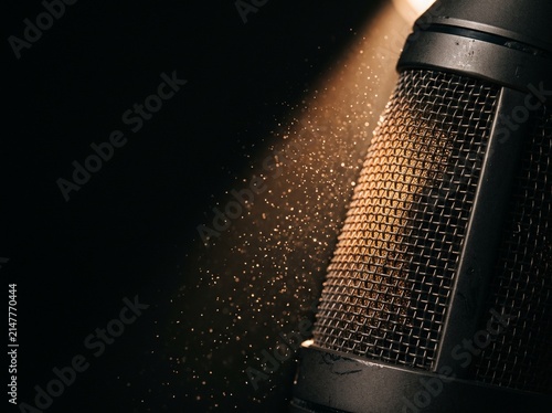 Close up of studio condenser microphone grill illuminated by spotlight in dark room
