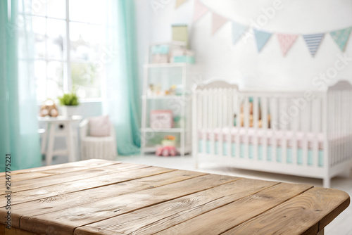 Rustic wooden table top surface with blurred bright white baby nursery background featuring soft pastel colors and natural morning light for product display and photography