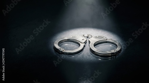 Handcuffs Spotlight: A pair of gleaming metal handcuffs rests under a dramatic spotlight, symbolizing justice, law, and consequence.