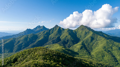 Panoramic Green Mountain Ridges Beneath Large White Clouds Under a Clear Bright Blue Sky