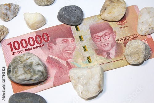 Obraz na plátne Indonesian 100,000 rupiah banknote surrounded by natural stones, symbolizing economic pressure, weak currency, inflation, financial hardship, and declining purchasing power