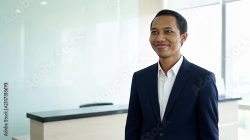 Indonesian business man investor, doubtful young male ceo executive wearing suit standing in office holding hand in chin looking away at work thinking on leadership question, feeling doubt.