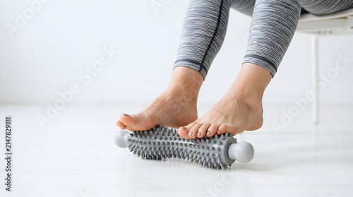 Women's feet on a needle roller for plantar fasciitis, reflexology self-massage, and myofascial release on a white background. AI generated.
