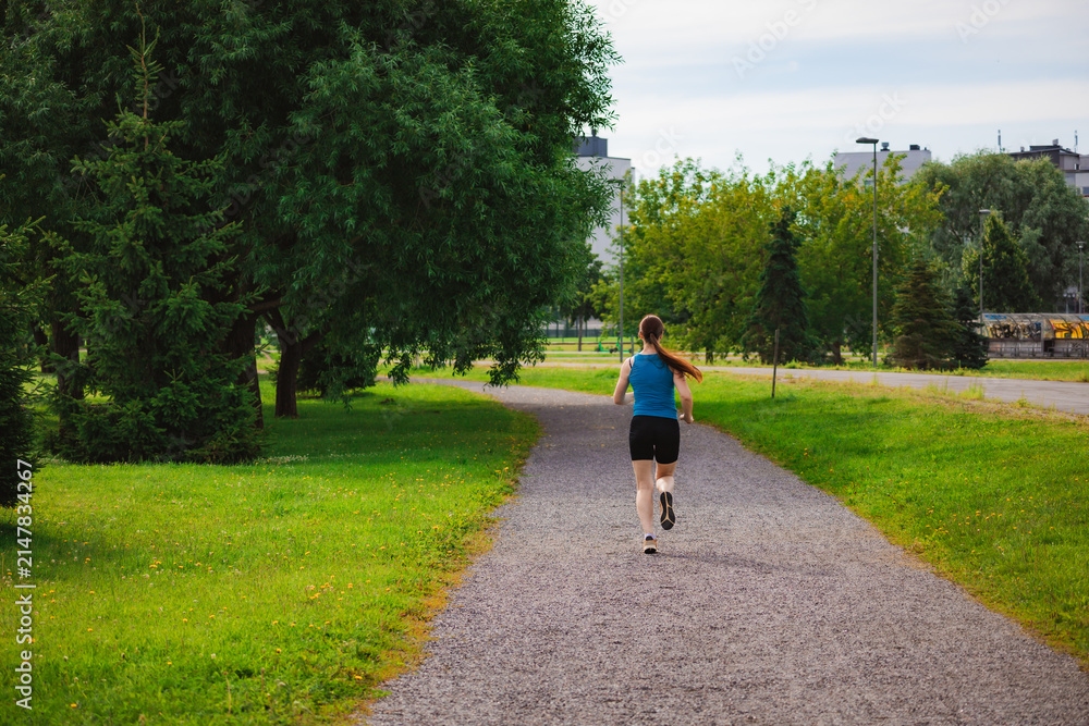 Fototapeta premium Woman Running in a Sunny Park During Morning Workout