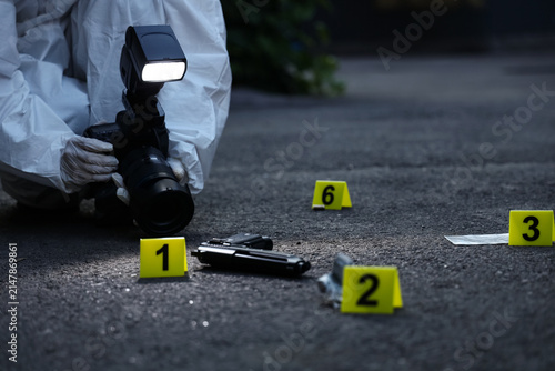Fotografía Forensic investigator in protective suit photographing crime scene evidence with