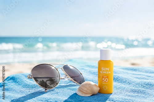 Sunglasses, seashell and sunscreen on towel, beach vacation and summer travel.