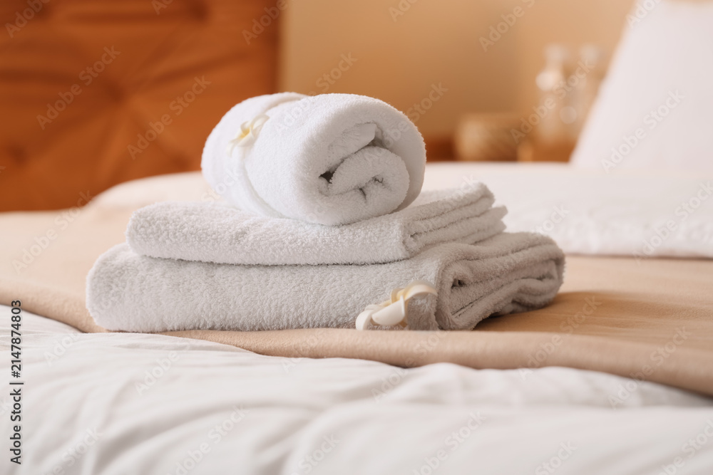 Fototapeta premium Stack of clean white towels with a decorative flower on a hotel bed, hospitality and comfort concept, this arrangement suggests a relaxing spa experience or a welcoming guest room
