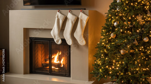 Stockings hang from a stone fireplace mantel next to a brightly decorated Christmas tree that glows with warm white lights in a cozy living room during the winter holiday season.