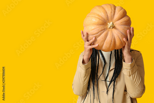 Beautiful young African-American woman with big pumpkin on yellow background