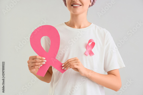 Young woman after chemotherapy with pink ribbons on light background, closeup...