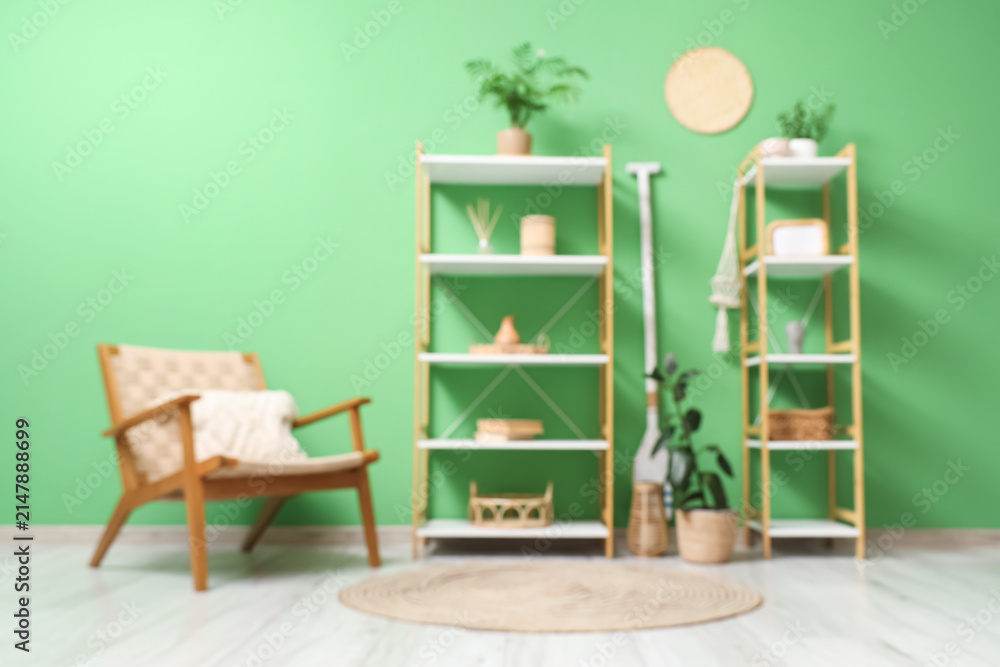 Fototapeta premium Blurred view of living room with shelving units and wooden armchair near green wall