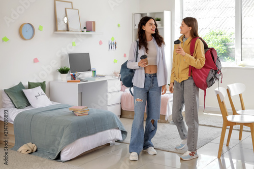 Female students with backpacks and cups of coffee in dorm room