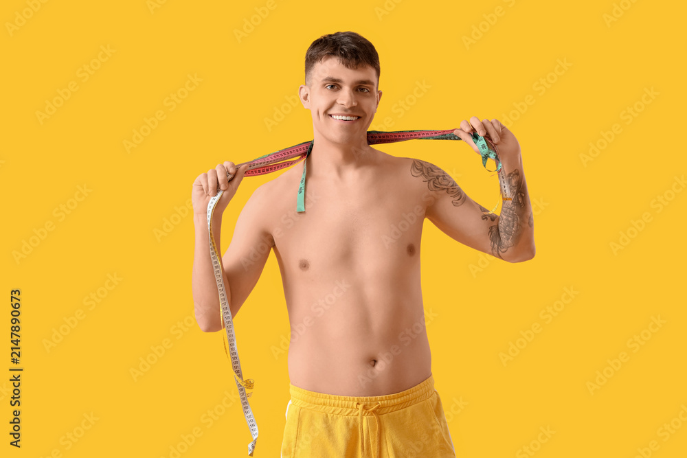 Fototapeta premium Young man with measuring tapes on yellow background. Weight loss concept