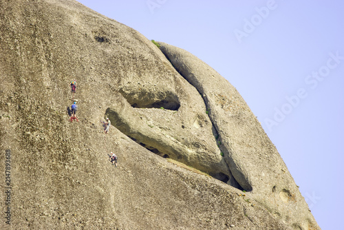 Cuadro en lienzo Four climbers ascend a sheer rock face under a clear blue sky.
