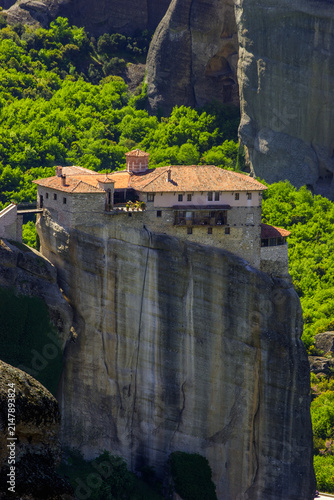 The Monastery of Agios Nikolaos Anapafsas perched on a rock formation in Meteora, Greece, surrounded by lush green trees under a clear sky.