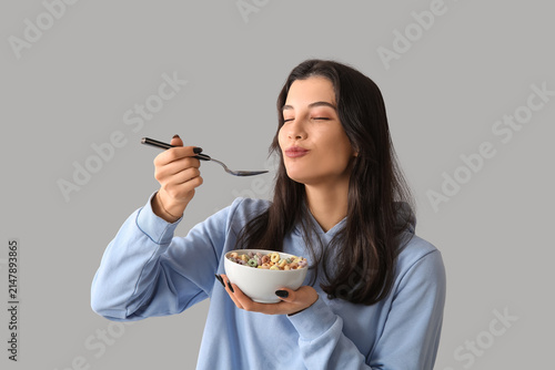 Young woman eating tasty cereal rings on light background