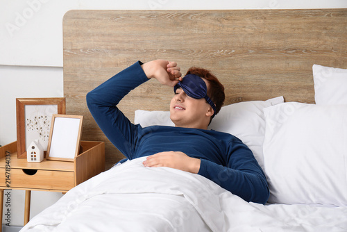 Morning of handsome young happy man in stylish pajamas on bed at home