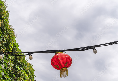 Traditional Red Chinese Lantern Hanging on String Lights Against Cloudy Sky.