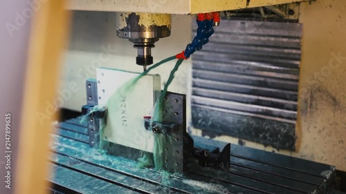 Wide shot of precision CNC milling machine drilling clamped block while spraying green cooling fluid during automated manufacturing process