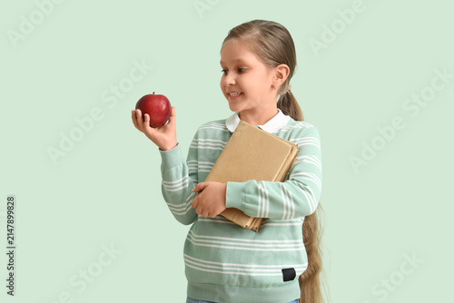 Little schoolgirl with books and apple on mint background
