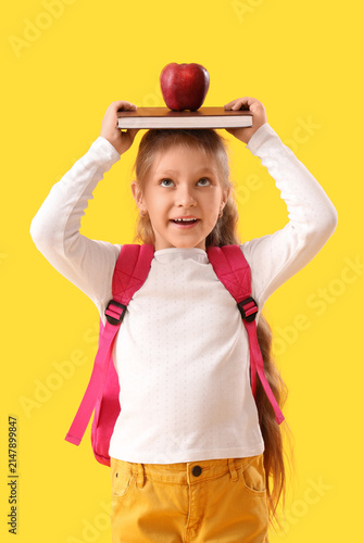 Little schoolgirl with book and apple on yellow background