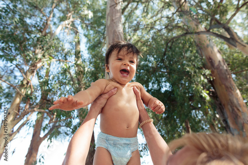 Fotografie Happy baby playing in arms outdoor among trees
