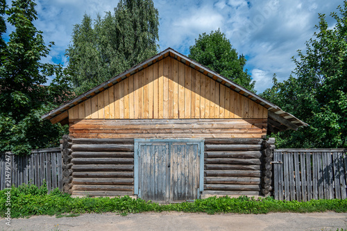 Old wooden shed or garage with a gable roof and a wooden fence on a rural street.