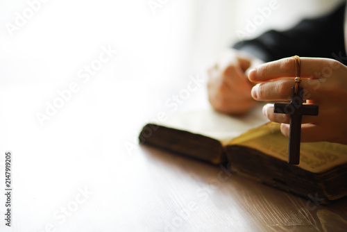 Фотография Hands Holding Wooden Cross Pendant Over Open Bible in Prayerful Reflection