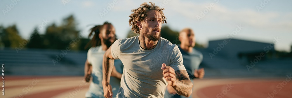 Fototapeta premium Male runner sprinting with competitors on outdoor track for athletic training banner and sports performance background design