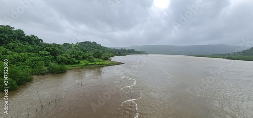 Vast River Flowing Through Lush Green Forested Hills Under Overcast Sky in Monsoon Landscape