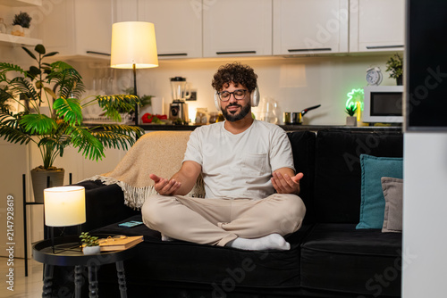 Quadro su tela Arabian man at home wears headphones listens to rain sound breathes deep eyes closed feels calm