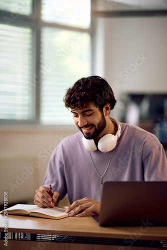 Happy college student writing notes while learning in classroom.