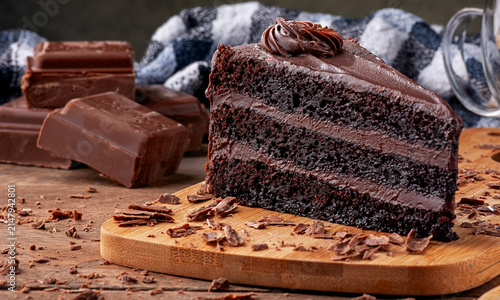 Canvas Print Rich decadent three layer chocolate cake slice on rustic wood board with shaving