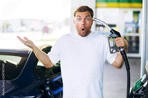 Quadro su tela Man with shocked expression holding a gas pump nozzle, indicating surprise and f