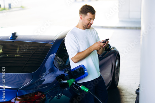 Foto Man filling up fuel tank at a gas station, checking phone for contactless paymen