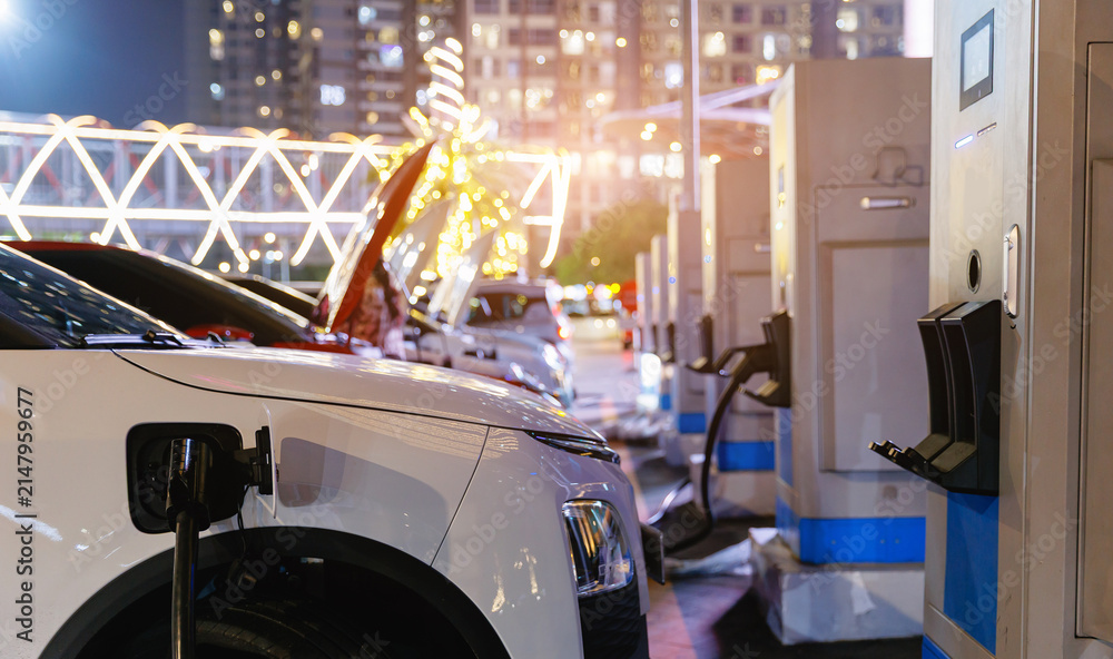 Naklejka premium Electric car vehicle plugged into Fast charger charging station at curbside.