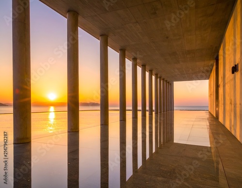 Concrete structure frames a sunset over tranquil water, reflecting the warm colors