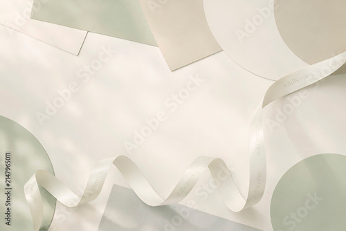 Minimalist flat lay with elegant white satin ribbon, soft pastel geometric paper shapes and delicate natural shadows. Premium neutral background with copy space for branding and modern design.