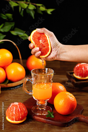 Fresh Blood Orange Juice Being Squeezed by Hand into Glass Mug with Citrus Fruits on Wooden Table