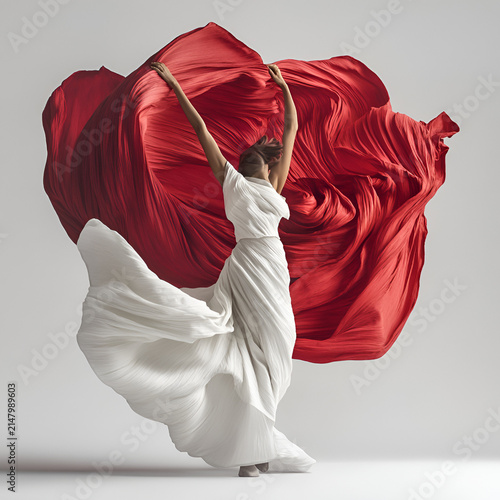 Elegant woman dancing in a flowing white dress set against a striking red fabric backdrop