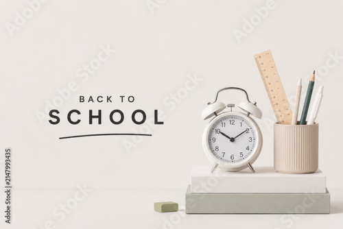Back to school concept with alarm clock and stationery. Education start theme featuring vintage timepiece and writing tools on white desk.